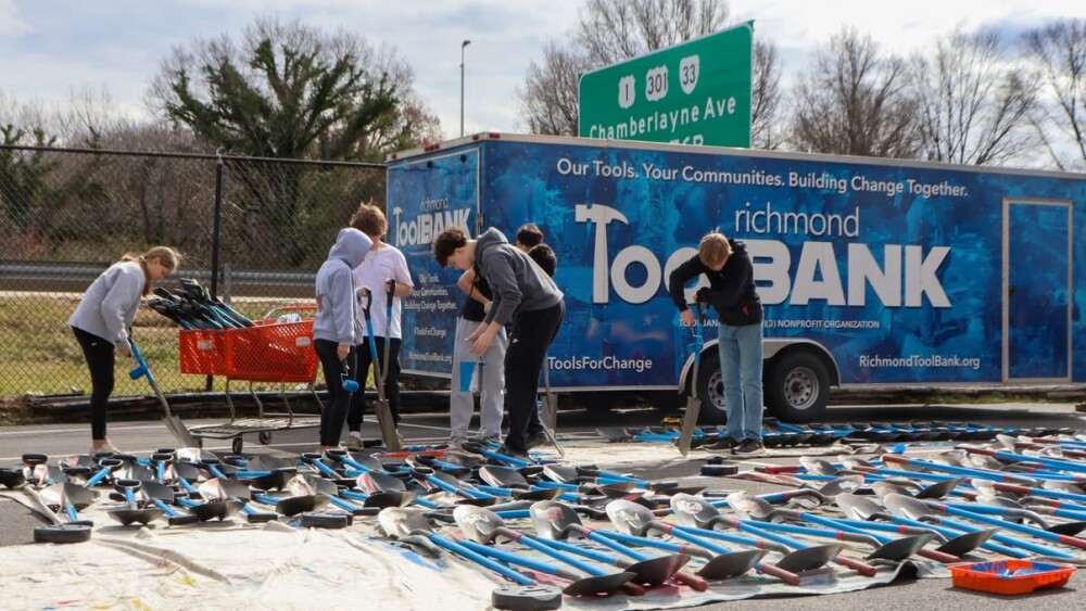 People stand over rows of shovels with blue handle; the shovels and people are in front of a blue "Richmond Toolbank" trailer truck