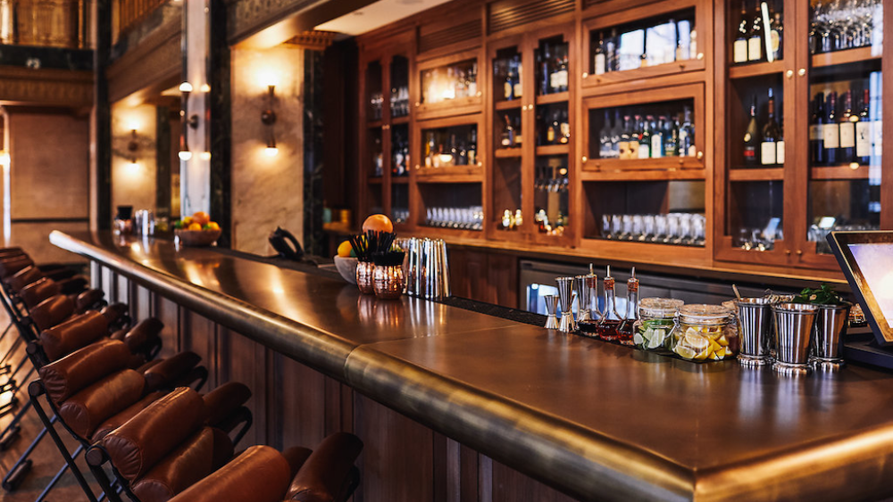 A sleek and clean bar area with high top seating and bottles tucked away in glass cases.