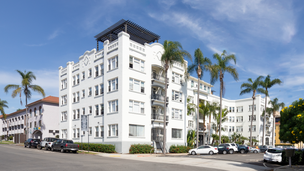 The Barcelona apartment building on Juniper Street in San Diego, with palm trees and cars parked out front. You can see its historic architecture — art deco and Spanish colonial — and the rooftop skydeck.