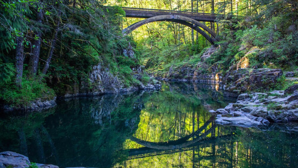 An arched bridge crosses a forested river canyon