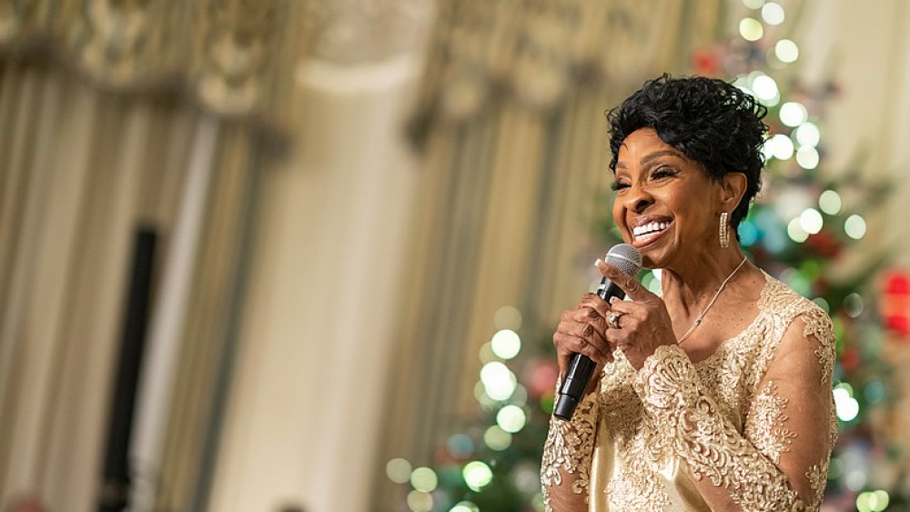 Gladys Knight performs at the White House. She is wearing a gold dress and smiling into a microphone.