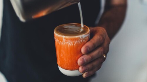 Coffee being poured into an orange ceramic mug
