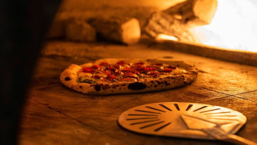 A pizza being cooked in Herb & Wood's wood-fire oven.