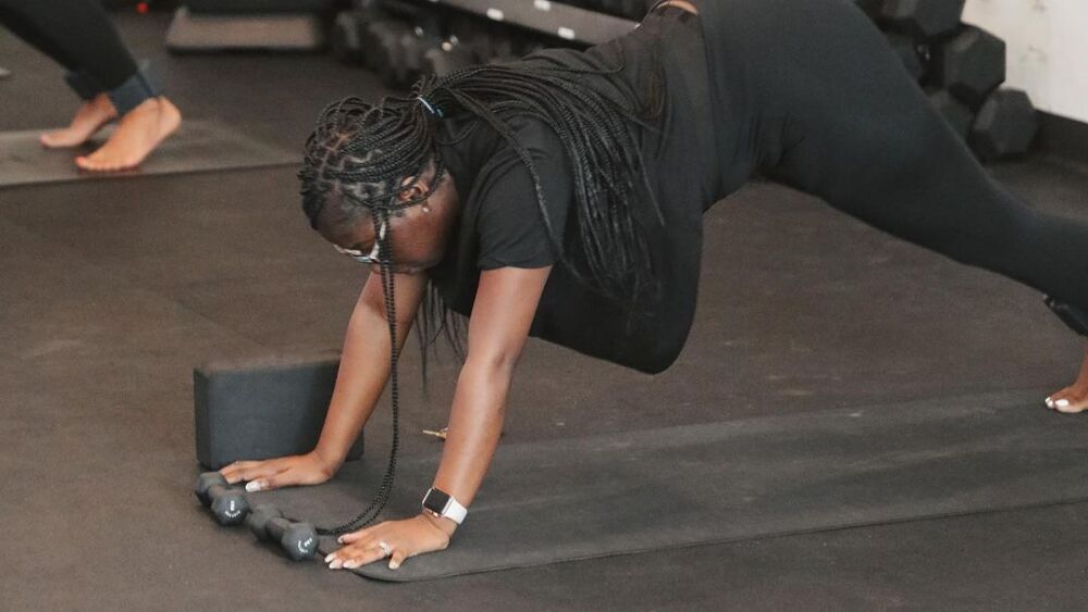 A woman in a yoga position on a yoga mat with weights nearby.