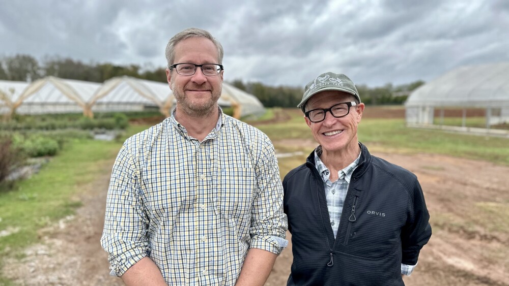 Two men smile for the camera outside on a produce farm.