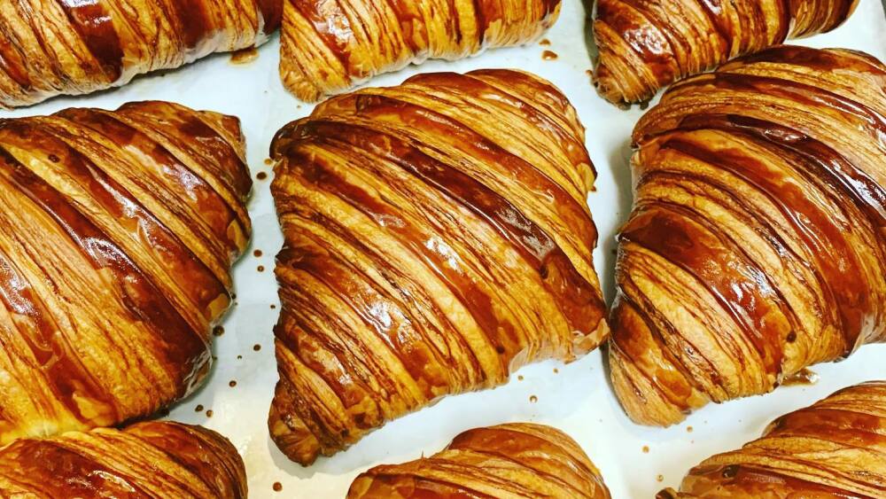 Freshly-baked croissants with stripey lamination spread out on a baking sheet.