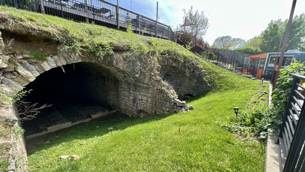 The opening of two gray stone caverns in a grass covered hill.