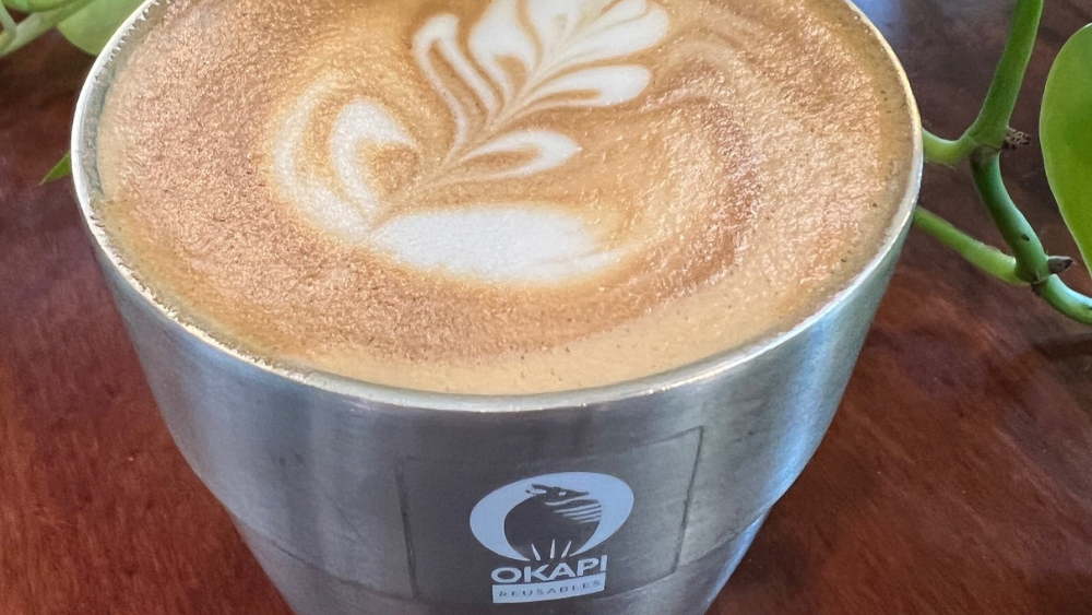 An aluminum mug filled with a coffee drink and topped with foam latte art.