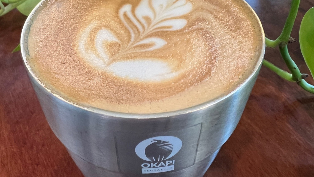 An aluminum mug filled with a coffee drink and topped with foam latte art. 