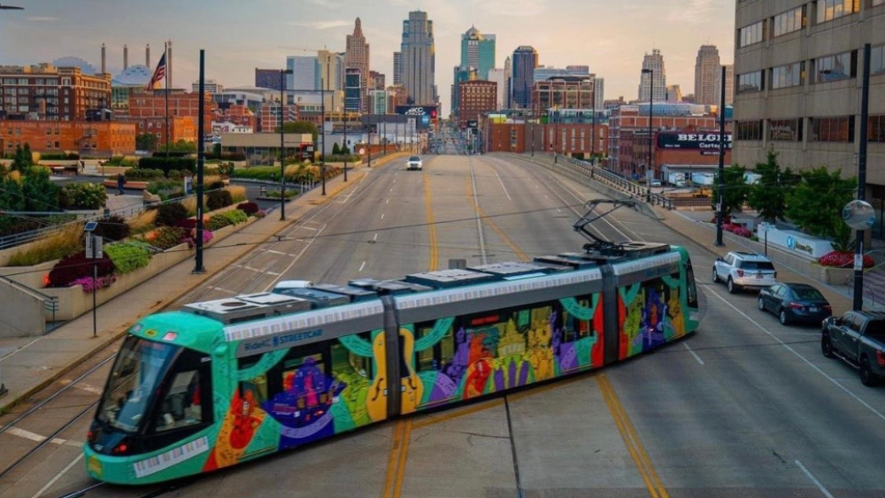 A colorful Streetcar sits diagonally on the road with the downtown Kansas City skyline in the distance.